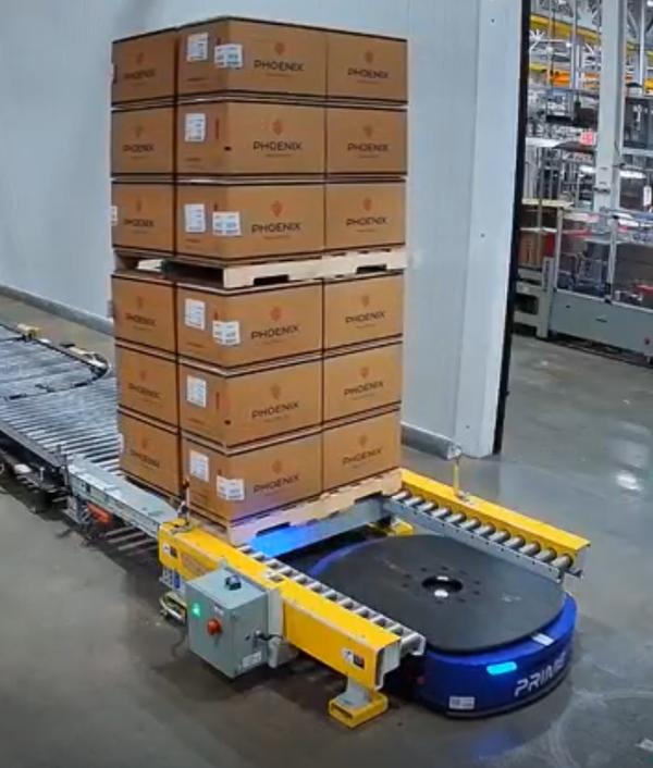 Prime MobilePallet AMR docking with a U-shaped pallet conveyor system — PLC-wrapped device integrated in a live PES workflow